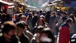 People wearing face masks to protect against the spread of the coronavirus walk though a shopping street Thursday, Dec. 31, 2020, in Tokyo. On the New Year's Eve, the shopping street is crowded by last minute shoppers who look for ingredients for …