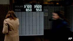 A woman looks at a sign announcing the price of the U.S. dollar and Brazilian real, in exchange for Argentine pesos, at a money exchange house in Buenos Aires, Argentina, Sept. 3, 2018. 
