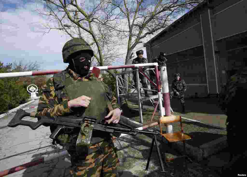 Ukrainian servicemen look on as an armed man, believed to be a Russian soldier, stands guard inside a Ukrainian military base in the Crimean town of Yevpatoria, March 5, 2014.