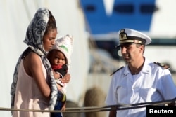 A woman holds a child after disembarking from the Italian Navy ship Borsini in the Sicilian harbour of Palermo, southern Italy, July 20, 2016.