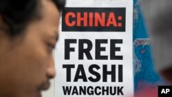 FILE - A Tibetan exile in Dharmsala, India, stands near a poster demanding that China release Tibetan activist Tashi Wangchuk, who was charged with inciting separatism, Jan. 27, 2017.