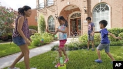 Vicky Li Yip sets up a bubble machine for her children, L to R, Kelsey, 8, Toby, 10 and Jesse, 5, outside their home, July 10, 2020 in Houston. She works from home and says online schooling has been exhausting, even with her husband helping out. (AP Photo/David J. Phillip)