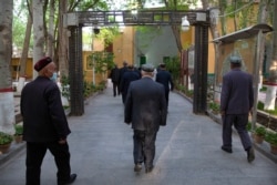 FILE - Uyghurs and other members of the faithful walk under an arch with security cameras as they leave after prayers at the Id Kah Mosque in Kashgar in western China's Xinjiang Uyghur Autonomous Region, April 19, 2021.