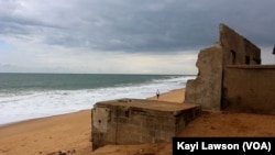 Un homme marche à côté des vagues sur la côte du village d'Afidégnigba au Togo, 19 septembre 2018. (VOA/Kayi Lawson)