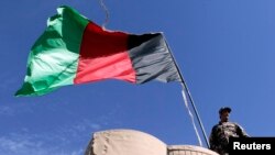 FILE - An Afghan National Directorate of Security (NDS) police stands guard next to an Afghanistan flag at a guard post of a police camp in Now Zad district in Helmand province, Afghanistan.