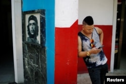 A young Cuban checks his phone at an internet hotspot next to a picture of late revolutionary hero Ernesto "Che" Guevara in Havana, Aug. 10, 2018.
