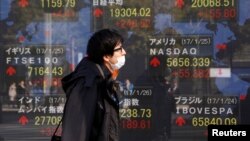 A man walks past an electronic board showing Japan's Nikkei average, top left, the Dow Jones average, top right, and the stock averages of other countries' outside a brokerage in Tokyo, Japan, Jan. 26, 2017. 