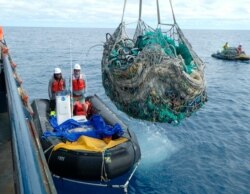 FILE - In this April 11, 2021, photo provided by Matt Saunter, Joao Garriques, left, and Matthew Chauvin load fishing nets onto a ship near Kure Atoll in the Northwestern Hawaiian Islands.