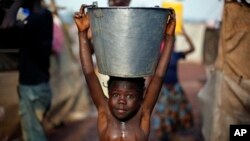 A child carrying a bucket full of water walks in mud after a storm in the airport camp in Bangui, Central African Republic, Sunday Feb. 2, 2014. Over 130,000 have seemed refuge outside the airport, living in dismal conditions, as fighting between Muslim 