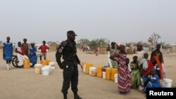 FILE - A Cameroonian police officer stands next to people waiting for water at the Minawao refugee camp for Nigerians who fled Boko Haram attacks in Minawao, Cameroon, March 15, 2016.