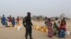FILE - A Cameroonian police officer stands next to people waiting for water at the Minawao refugee camp for Nigerians who fled Boko Haram attacks in Minawao, Cameroon, March 15, 2016.