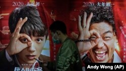 Seorang pria mengenakan masker untuk mengurangi penyebaran virus corona melintas di depan poster film di Poly Cinema, di Beijing, China, 25 Februari 2021. (Foto: Andy Wong/Associated Press)