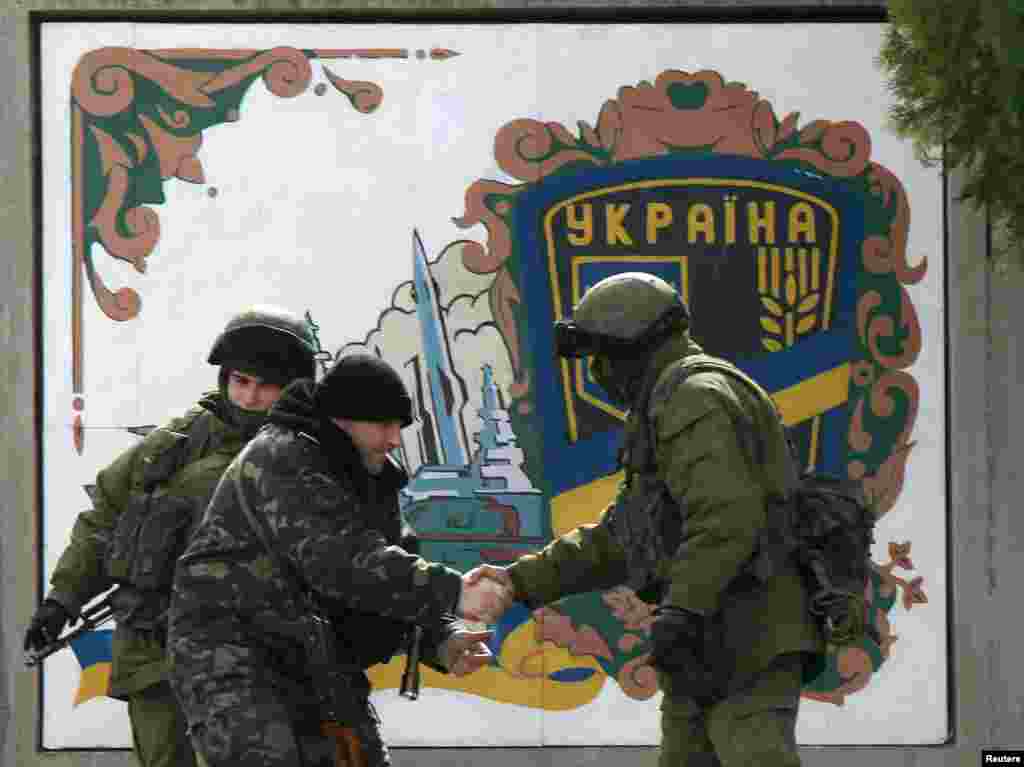 A Ukrainian serviceman (2nd L) shakes hand with an armed man, believed to be a Russian serviceman, at the Ukrainian military base in the village of Perevalnoye near the Crimean city of Simferopol. Crimea&#39;s pro-Russian prime minister will give people living there the choice of taking Russian or Ukrainian passports if the Ukrainian territory becomes part of Russia in a March 16 referendum.