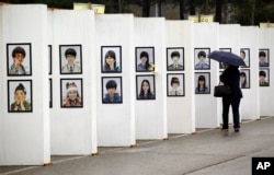 FILE - A woman looks at caricatures of the victims of the sunken ferry Sewol outside a group memorial altar in Ansan, South Korea, Thursday, April 16, 2015. Tears and grief mixed with raw anger Thursday as black-clad relatives mourned the 300 people, mostly high
