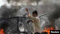 Seorang pekerja konveksi di tengah kobaran asap menyusul bentrokan antara polisi dengan demonstran yang menuntut kenaikan upah (3/1) di Phnom Penh. 