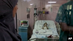 In this March 5, 2018 photo, Syrian refugee Sara al-Matoura, watches through a window at her one-year-old daughter Eman's chest heaving up and down under a tangle of medical wires at a hospital in Amman, Jordan. (AP Photo/Raad Adayleh)