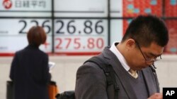 People stand by an electronic stock board of a securities firm in Tokyo, Dec. 3, 2018. Shares are advancing in Asia following the meeting between Presidents Donald Trump and Xi Jinping.