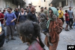 Seorang perempuan Palestina yang berlumuran debu dan kotoran menggendong seorang anak, saat pertempuran sengit antara Israel dan gerakan Hamas berlanjut selama enam hari berturut-turut di Kota Gaza pada 12 Oktober 2023. (Foto: AFP)