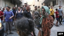A Palestinian woman covered in dust and dirt carries a child, as raging battles between Israel and the Hamas movement continue for the sixth consecutive day Gaza City on Oct. 12, 2023.