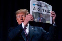 President Donald Trump holds up a newspaper with the headline that reads "ACQUITTED" at the 68th annual National Prayer Breakfast, at the Washington Hilton, Feb. 6, 2020, in Washington.