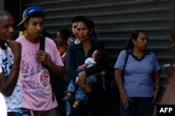A woman holds her baby while queuing outside a supermarket in Caracas to buy basic food and household items, Nov. 10, 2017. In crisis-stricken Venezuela, the cost of the basic basket of goods soared to nearly 2.7 million bolivars in September, the equivalent of six minimum monthly wages.