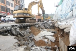 An excavator fixes the road after three cars were swallowed by a sinkhole on the side of the street by a construction location by Olympic Stadium while it was raining this afternoon in Phnom Penh on Wednesday, June 8, 2016. (Leng Len/VOA Khmer)