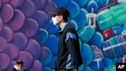 A pedestrian wears a face mask as he walks past a mural of a fish while strolling on the boardwalk at Coney Island, April 2, 2020, in the Brooklyn borough of New York.