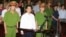Cu Huy Ha Vu (C) stands between policemen in the dock during his trial at a court in Hanoi, August 21, 2011.