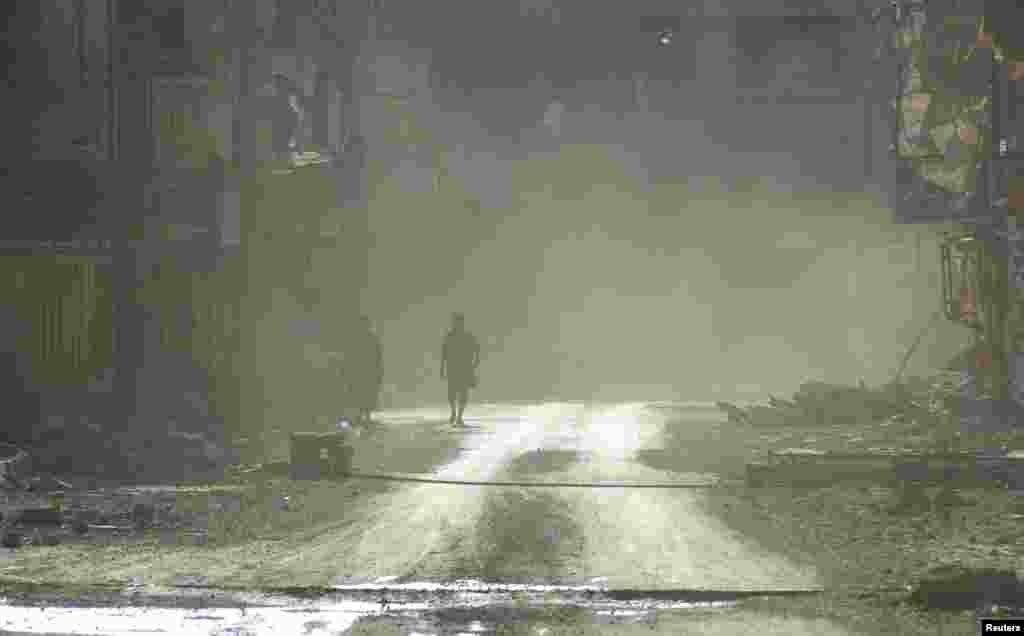 Para anggota Tentara Pembebesasan Suriah di tengah asap di sebuah jalan yang hancur dan dipenuhi puing-puing di Deir al-Zor, Suriah (22/7).