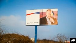 FILE - A partially damaged billboard with a portrait of Russian President Vladimir Putin is seen on a roadside near Simferopol, Crimea, Jan. 24, 2016. The billboard reads: "Crimea. Russia. Forever."
