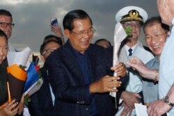 FILE - Cambodia's Prime Minister Hun Sen, center, gives a flower to a passenger who disembarked from the MS Westerdam, owned by Holland America Line, at the port of Sihanoukville, Cambodia, Feb. 14, 2020.