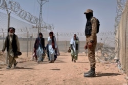 FILE - In this Aug. 20, 2021, file photo, Pakistani army soldier stands guard while Afghan people enter into Pakistan through a border crossing point, in Chaman, Pakistan. Chaman is a key border crossing between Pakistan and Afghanistan.