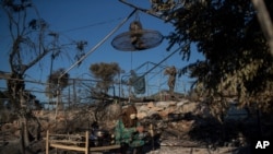 A migrant woman sits on a burned bed in the Moria refugee camp on the island of Lesbos, Greece, Sept. 10, 2020. A second fire in Greece's notoriously crowded Moria refugee camp destroyed nearly everything that had been spared in the original blaze.