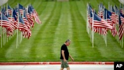 A man walks past a row of flags as he visits a park, Friday, May 15, 2020, in Kansas City, Missouri.