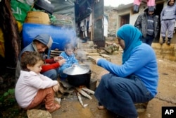 FILE - A Syrian refugee woman with her children prepares food near her tent in a camp for Syrians who fled their country’s civil war, in the Chouf mountain town of Ketermaya, Lebanon.