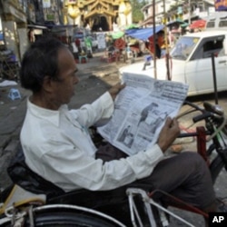 A Burmese man reads a newspaper reporting on the elections as he waits for trishaw passengers.