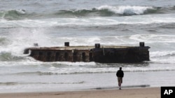 FILE - A man looks at a 70-foot-long dock with Japanese lettering that washed ashore on Agate Beach in Newport, Ore., June 6, 2012.