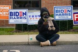 A voter sits on the sidewalk as voters wait in long lines to cast their ballots during early voting at St. Luke's United Methodist Church in Indianapolis, Oct. 28, 2020. The wait to vote was over 4 hours.