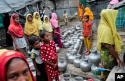 FILE - Rohingya women and children wait in a line to collect water at the Leda camp, an unregistered camp for Rohingya in Teknaf, Bangladesh.