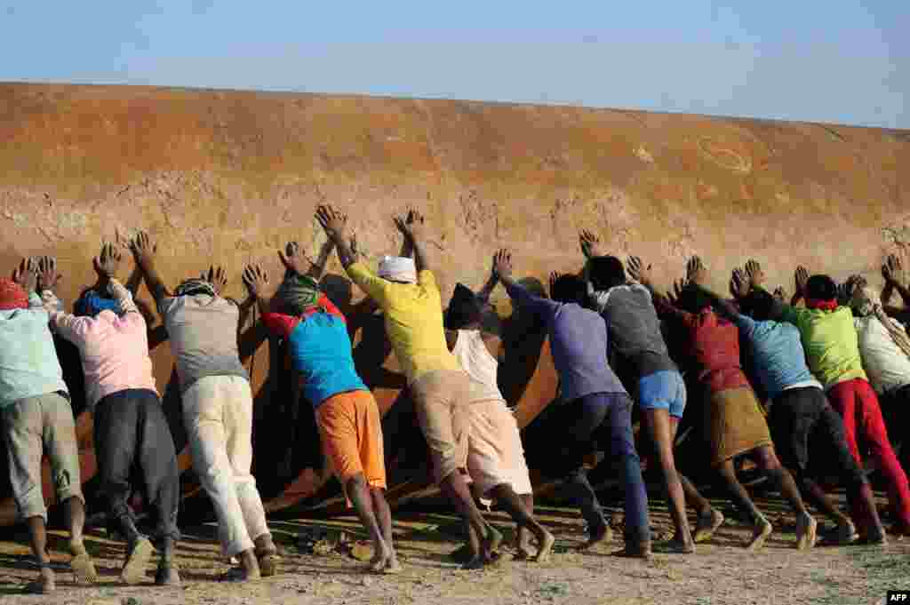 Indian laborers push a pontoon to construct a temporary pontoon bridge over the River Ganges for the upcoming Magh Mela festival in Allahabad.
