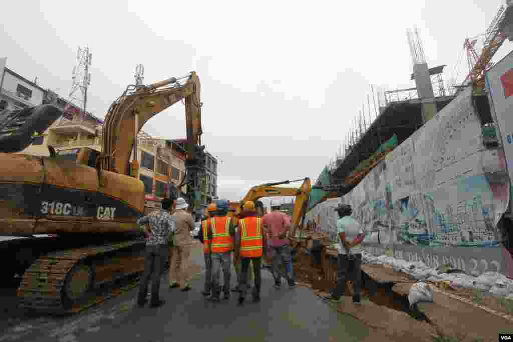 កម្មករ​សំណង់​ឈរ​មើលរថ​យន្ត​អេស្កា​វាទ័រ​ជីក​កកាយ​ដី​បន្ទាប់​ពី​រថយន្ត​បី​​គ្រឿង​ផុង​ស្រុត​ ខណៈពេល​មាន​ភ្លៀង​ធ្លាក់​ជោគជាំ​​នៅ​ការដ្ឋាន​​សំណង់​​នៅ​​ជាប់​របង​ពហុកីឡា​ដ្ឋានជាតិ​​អូឡាំពិក ​ខណ្ឌ​ប្រាំពីរ​មករា ​នៅ​ថ្ងៃ​ពុធ​ទី​០៧​ខែ ​មិថុនា​ ឆ្នាំ​២០១៦​នេះ​។ ​រថយន្ត​ចំនួន​បី​គ្រឿង​ដែល​គេ​ចត​ចោល​នៅបណ្ដោយ​ផ្លូវ​ជាប់​​ការ​ដ្ឋាន​នេះ ត្រូវ​ក្រុម​ហ៊ុន​ការដ្ឋាន​សាងសង់​ស្ទួច​ទៅ​​ឲ្យ​ម្ចាស់​ដើម​វិញ​។ ​(ឡេង ឡែន/VOA)