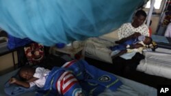 Seorang anak yang menderita malaria tidur di bawah kelambu sementara seorang ibu menyusui di sini anak, juga menderita malaria, di rumah sakit Siaya di Kenya Barat. (Foto: AP)