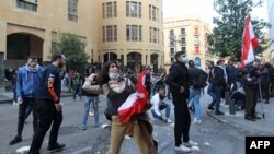 A Lebanese demonstrator hurls rocks over a fortified gate, leading to the Lebanese Parliament building, in downtown Beirut, March 13, 2021, during a protest against the political system.
