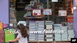 A young girl wearing a face mask walks past a store displaying a coronavirus information poster and selling children's school stationery, backpacks, protective masks and hand sanitizers in Madrid, Spain, Monday, Aug. 24, 2020.