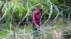 A woman looks through four-foot (1.2-metre) high coils of razor wire that divide the Russian-backed breakaway territory from Georgian-controlled land in village of Khurvaleti in Georgia, July 25, 2013.