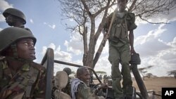 A Kenyan army soldier, left, looks up as a Somali government soldier, right, climbs across the vehicle that they are sharing, and another Somali government soldier prepares to drive, center, in Tabda, inside Somalia, February 20, 2012.