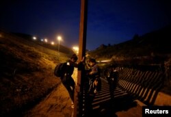 FILE - Migrants from Honduras, part of a caravan of thousands from Central America trying to reach the United States, jump the fence to cross it illegally into San Diego County, U.S., taken from the border wall in Tijuana, Mexico, at right, Jan. 16, 2019.