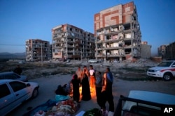 In this photo provided by the Iranian Students News Agency, ISNA, survivors of the earthquake warm themselves in front of destroyed buildings at the city of Sarpol-e-Zahab in western Iran, Monday, Nov. 13, 2017.