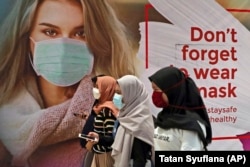 Wanita bermasker melewati iklan yang mempromosikan kesadaran akan wabah virus corona di sebuah pusat perbelanjaan di Jakarta, Rabu, 1 Juli 2020. (Foto: AP/Tatan Syuflana)
