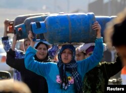 Women carry gas cylinders to fill them at a distribution point in Cairo, Jan. 19, 2015.